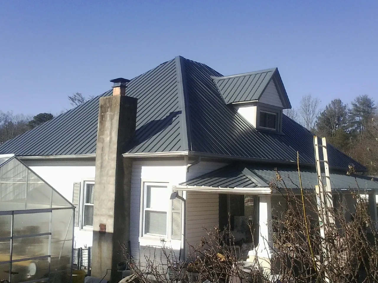Dark blue standing seam metal roof on a white farmhouse with dormer — Slate & Tile Roof Repair by Roofing Brothers in East Wakefield