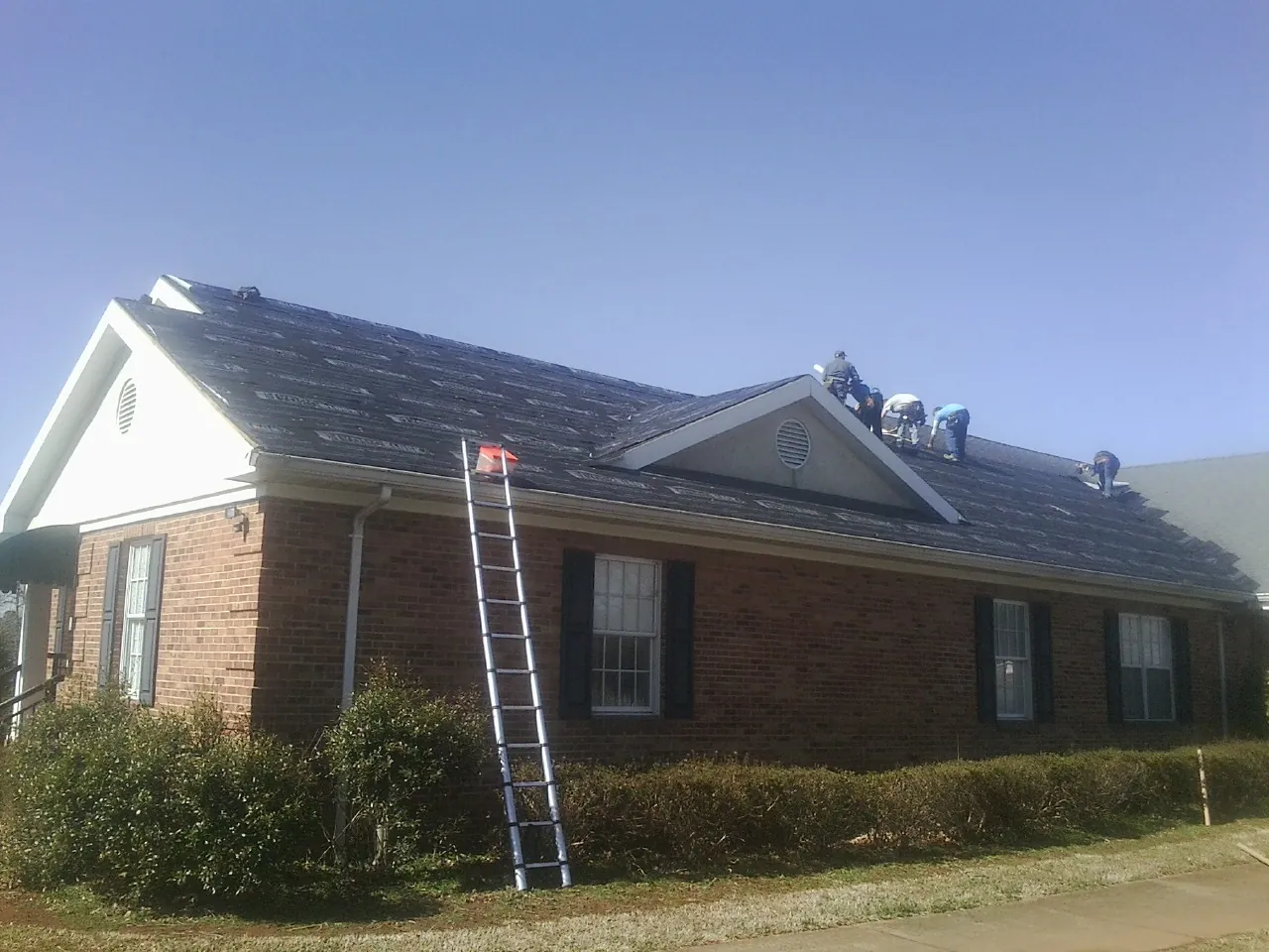 Crew tearing shingles off a brick ranch roof with a ladder set — Emergency Roof Repair work by our crew in East Wakefield