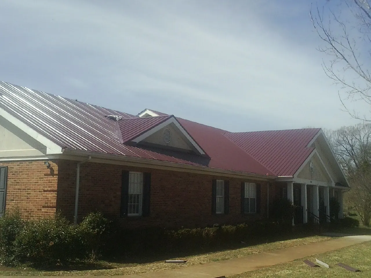 Red metal roof with gabled entries on a long brick building, from a Hail Damage Roof Repair job in East Wakefield