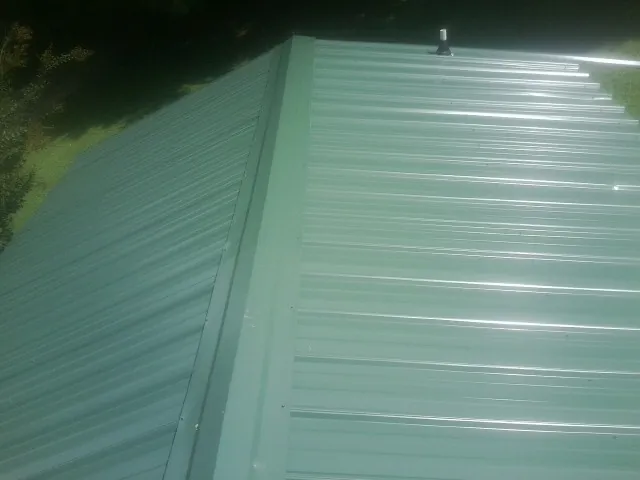 New green metal panels meeting at the ridge of a roof — Flat Roof Repair work by our crew in East Wakefield