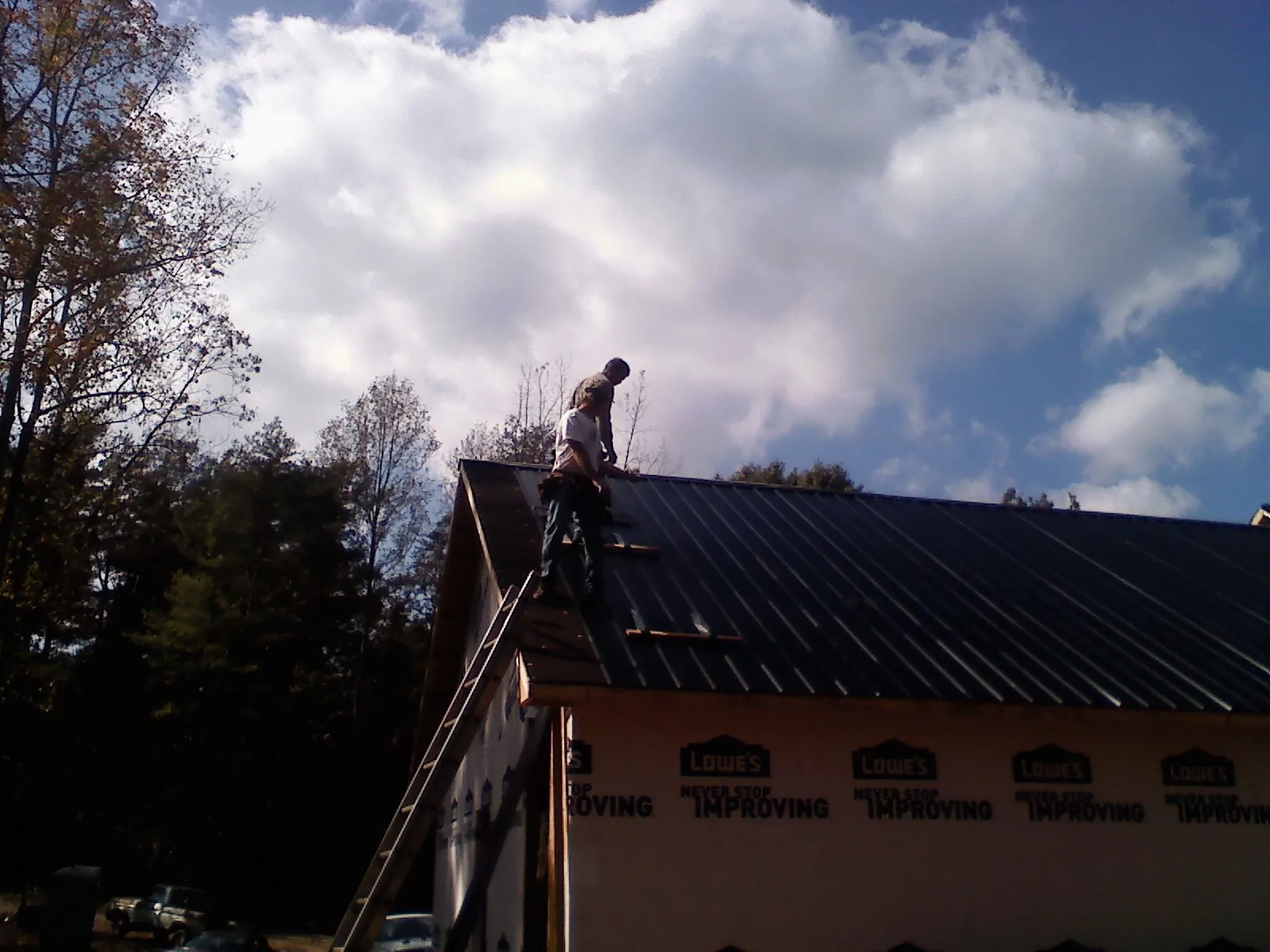Roofer fastening dark metal panels high against a cloudy sky, from a Roof Inspection job in East Wakefield
