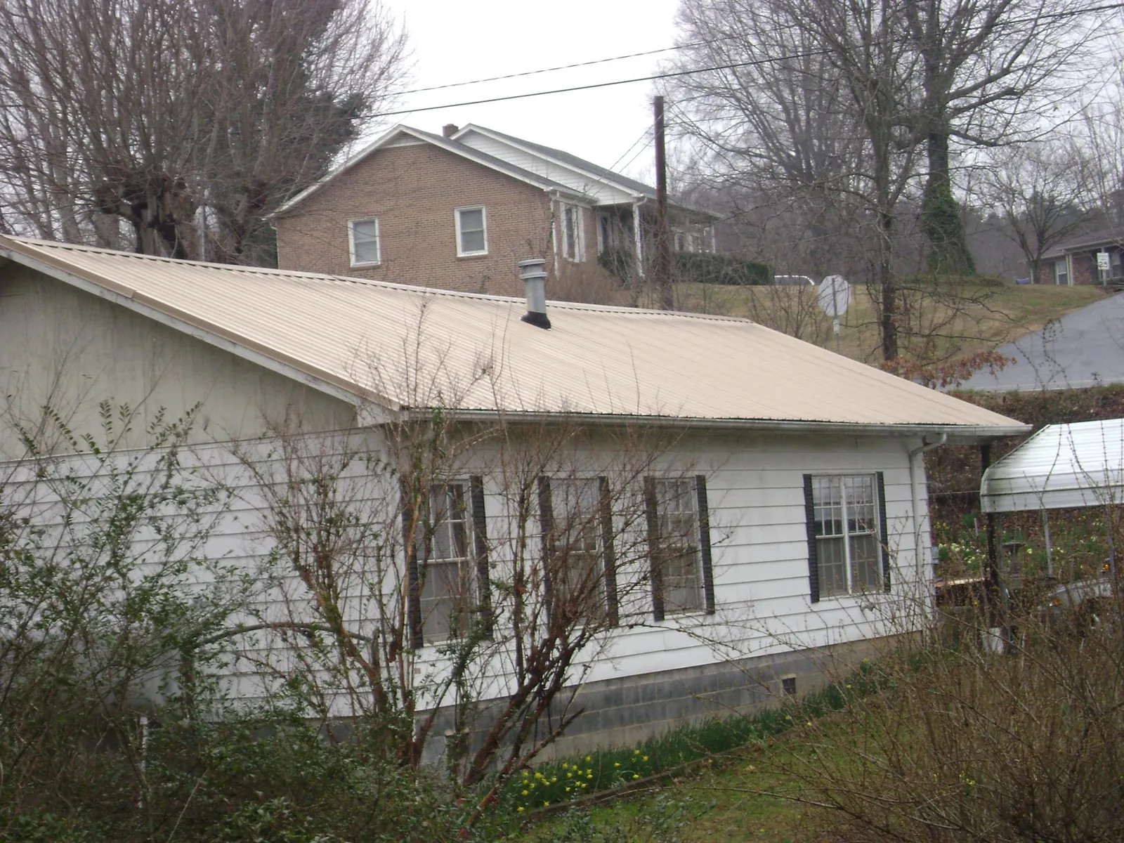 Tan metal roof on a white sided house set into a hillside — Commercial Roofing by Roofing Brothers in East Wakefield